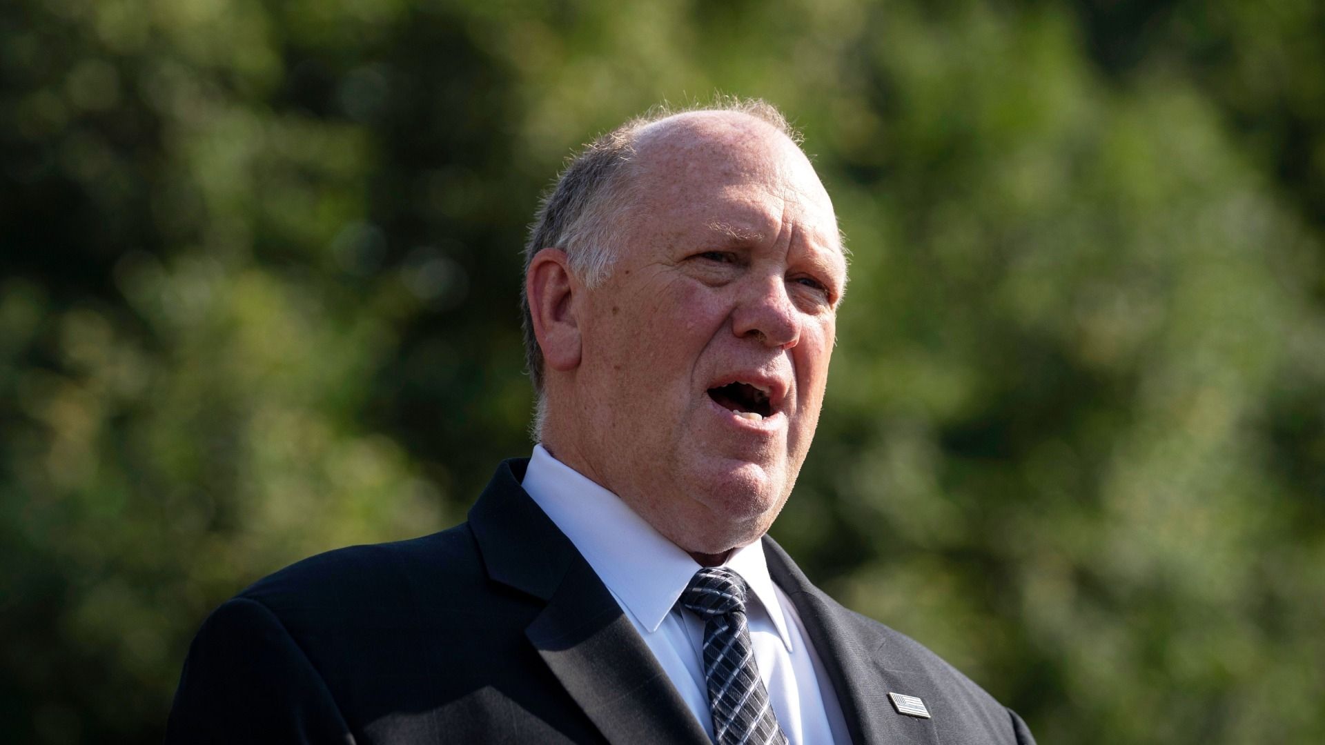 Tom Homan viste traje y corbata oscuros mientras habla
