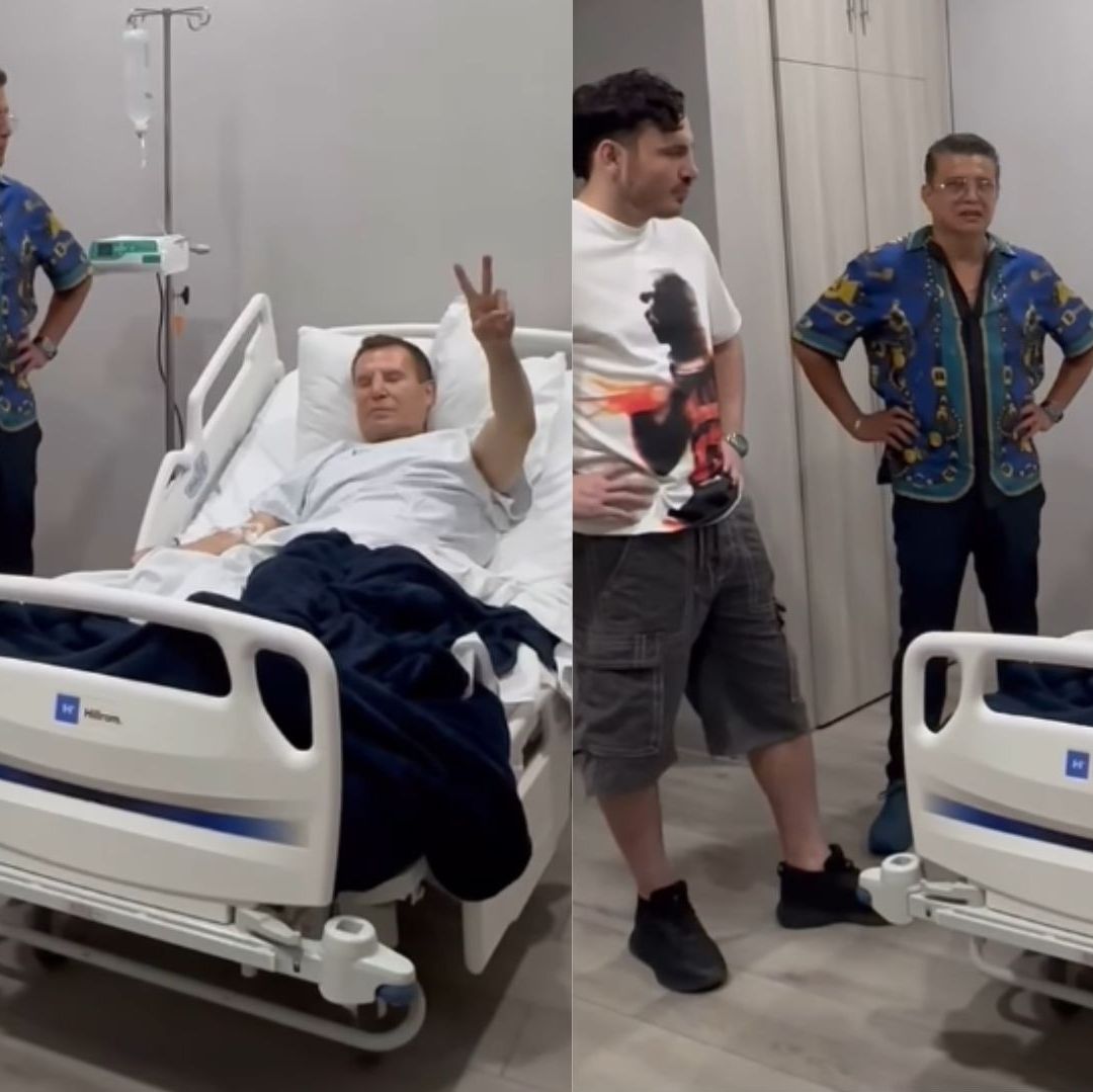 Un hombre se encuentra en un hospital acostado en una cama, hace una señal de saludo.