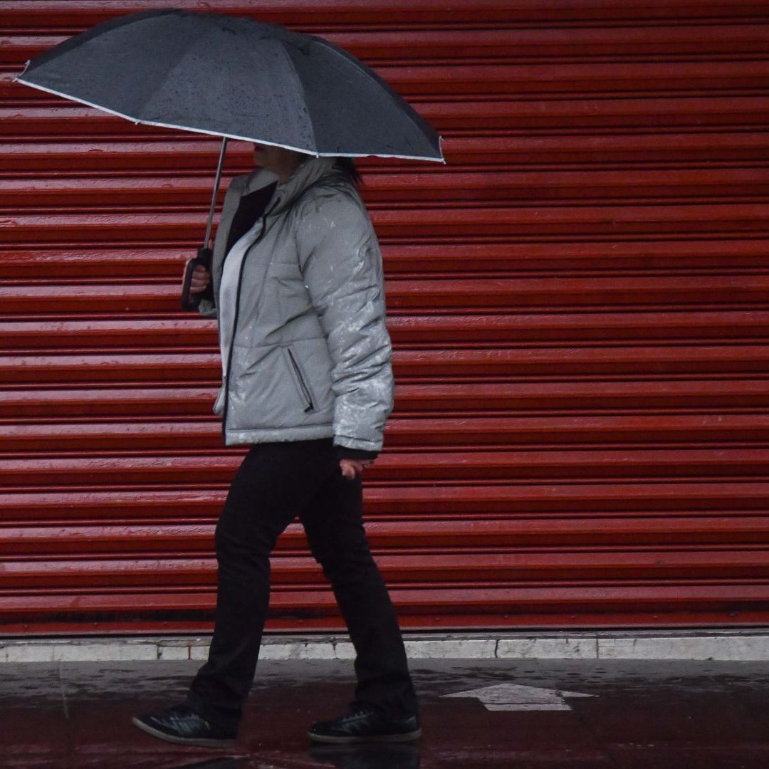 Un bombre camina protegiéndose de la lluvia con una sombrilla
